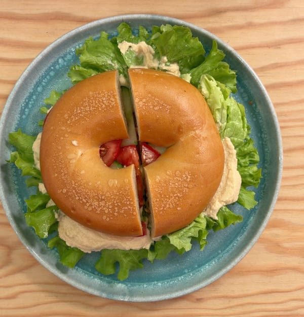 Bagel mit Frischkäse, Salat und Tomate auf einem blauen Teller