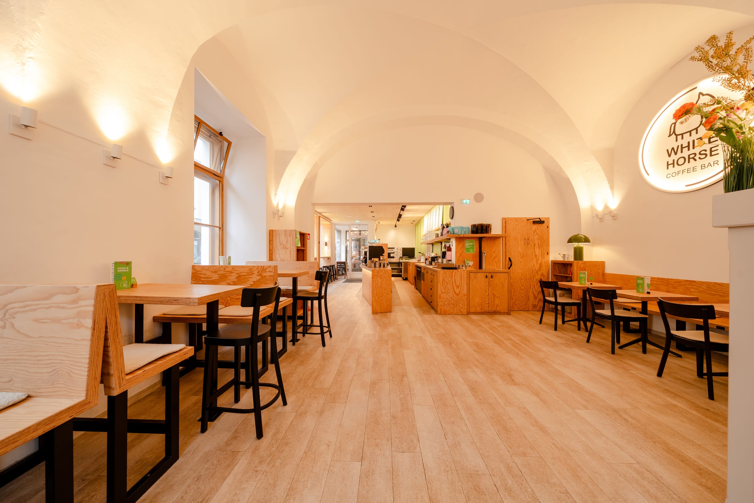 Weiter Blick durch den Gastraum des White Horse Coffee Bar mit Sitzbänken, Theke im Hintergrund und beleuchtetem Logo-Schild rechts