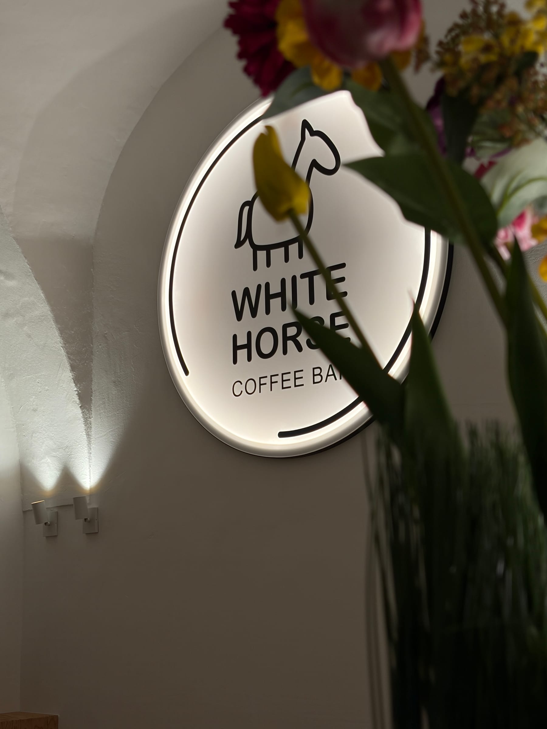 Leuchtendes White-Horse-Logo-Schild an der Wand, im Vordergrund Blumen