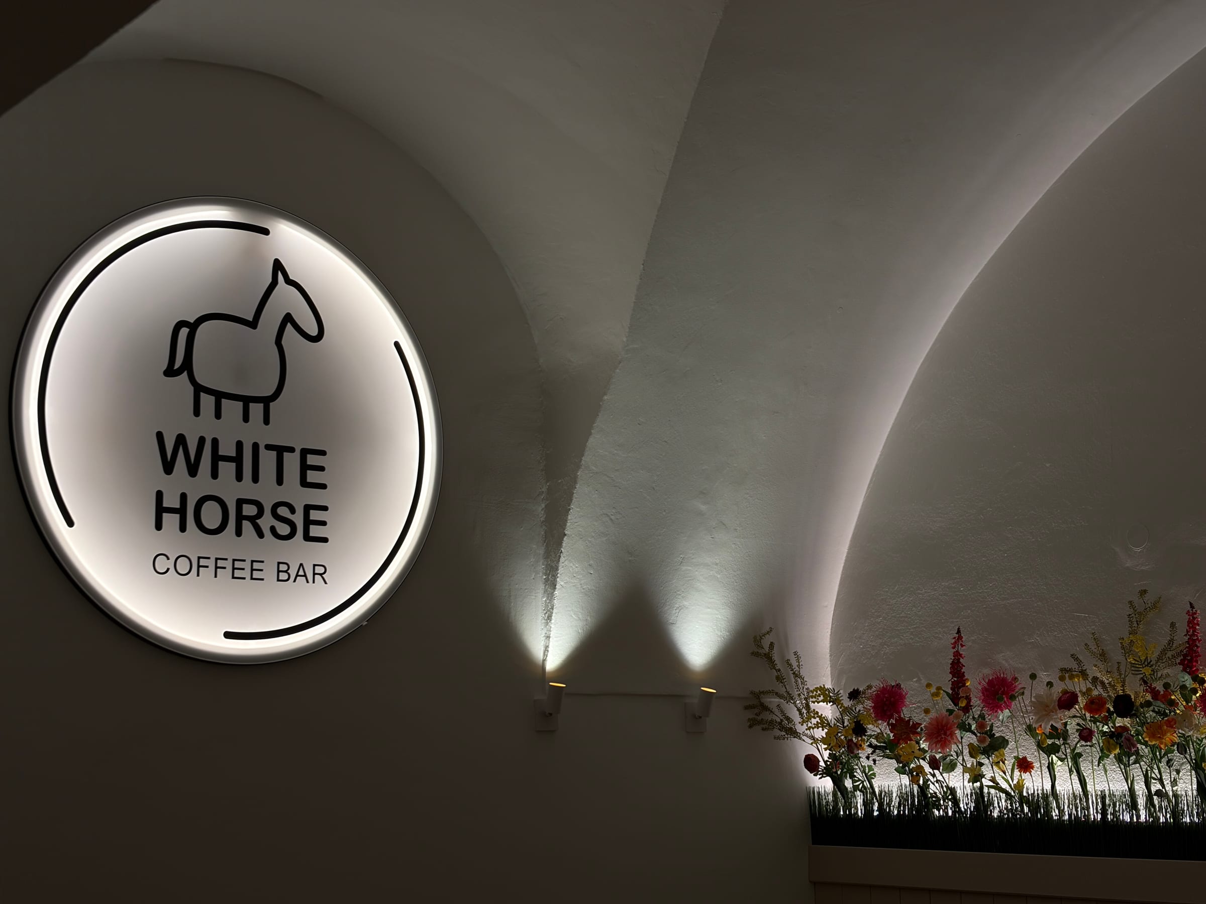 Beleuchtetes White-Horse-Logo an der Wand im Eingangsbereich mit Blumendekoration